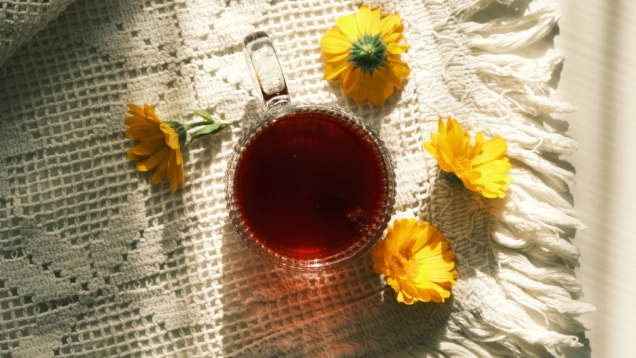 Ein Glas Tee auf einer Tischdecke mit Blumen im Flat Lay Stil fotografiert zum genießen in den ersten Herbsttagen