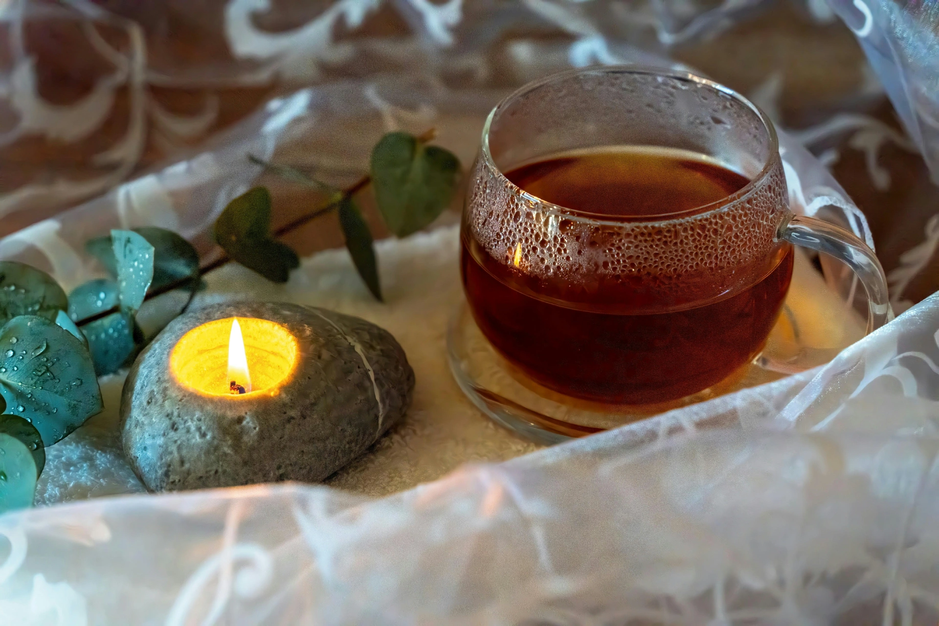 Teetasse aus Glas neben einem Teelicht und Eukalyptuszweig