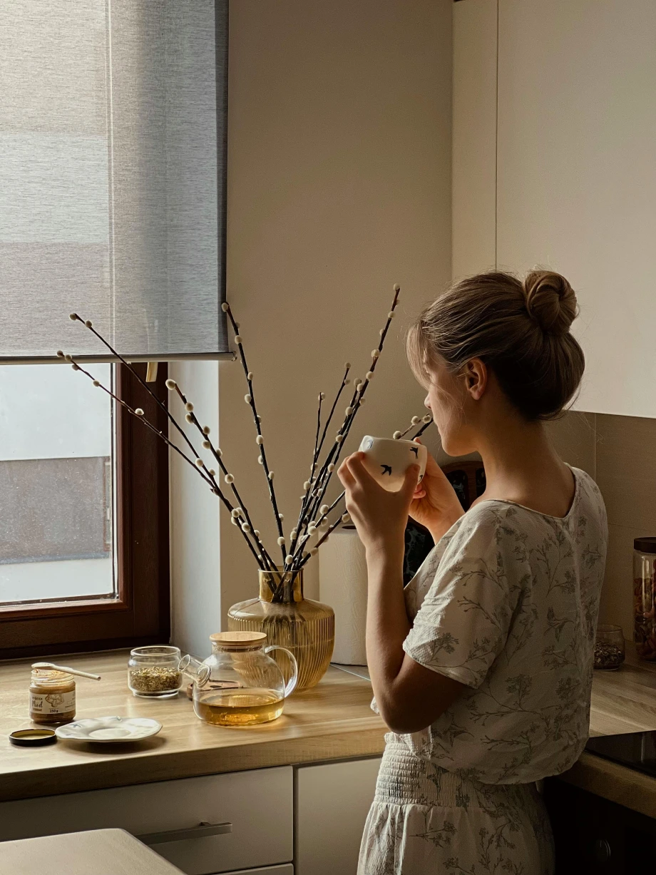 junge Frau genießt ihren frisch aufgegossenen Tee in einem Teeglas am Fenster